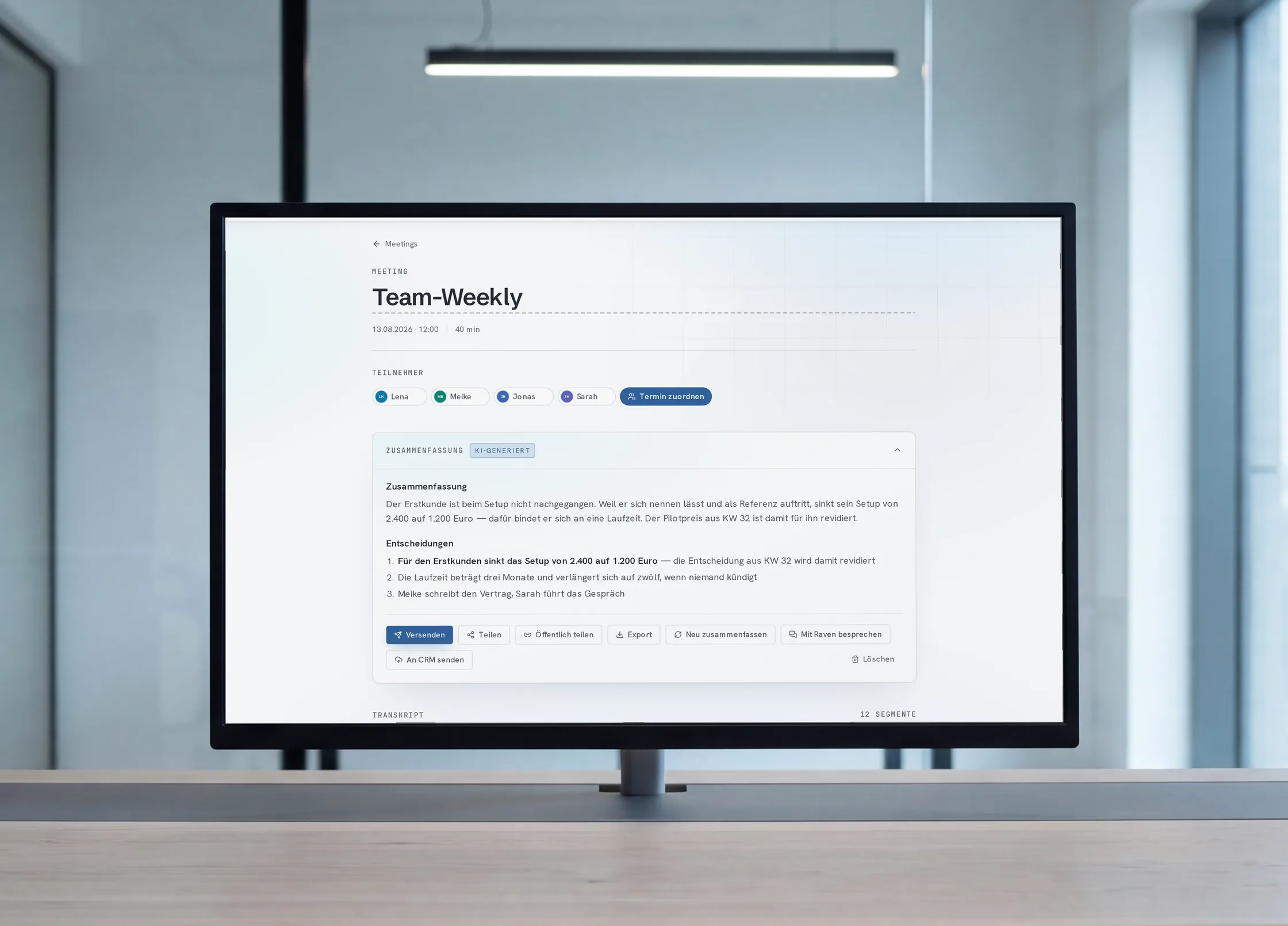 Monitor auf einem Eichentisch in einem hellen Büro; auf dem Schirm das fertige Raven-Protokoll „Team-Weekly“ mit Zusammenfassung