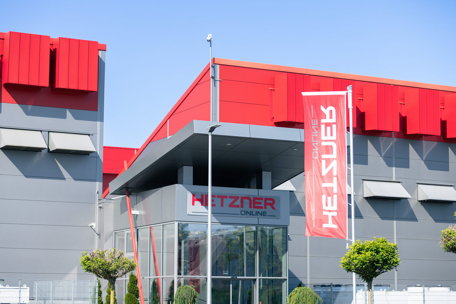 Eingang eines Hetzner-Rechenzentrums in Falkenstein: graue Fassade mit roten Blenden, Vordach über dem verglasten Empfang, Schriftzug „Hetzner Online“ über der Tür